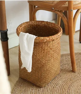 Handwoven straw storage basket detail, rustic style wastepaper basket with white cloth decor.