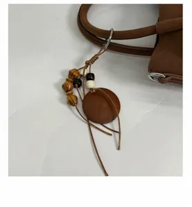 Brown suede tote bag pendant detail, vintage casual handbag accessory with wooden beads charm.
