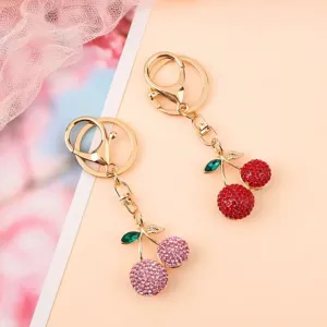 Primer plano detallado de llaveros de cereza con pedrería brillante y dijes de bolso de metal.