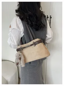 Detailansicht der eleganten Wildleder-Umhängetasche mit braunen Lederriemen und Plüschanhänger.