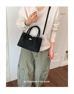 Detailaufnahme einer schwarzen Handtasche aus Kunstleder mit Metallverschluss und Griff.