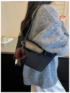 Detailansicht einer schwarzen Umhängetasche mit flauschigem Bommel und schickem Design.