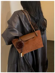 Nahaufnahme der braunen Wildleder-Umhängetasche mit flauschigem Bommel und Lederlasche.
