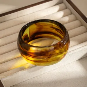 Dettaglio ravvicinato di bracciale rigido largo in resina con effetto ambra vintage.