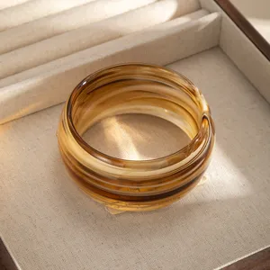 Dettaglio di bracciale rigido largo in resina effetto ambra rétro, elegante accessorio.