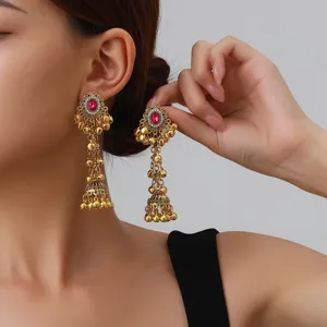 Close-up detail shot of vintage gold-tone jhumka earrings with red stone and dangling bells.