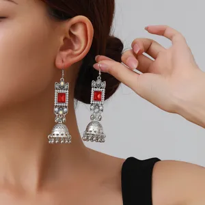 Close-up detail of vintage silver drop earrings with red square crystal and bell tassels.