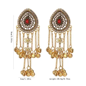 Detailed shot of gold tone teardrop tassel earrings with bells and red stone accent.