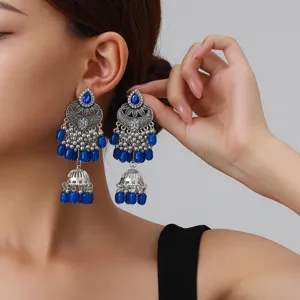 Gros plan détaillé de boucles d'oreilles jhumka argentées ethniques vintage avec perles bleues.