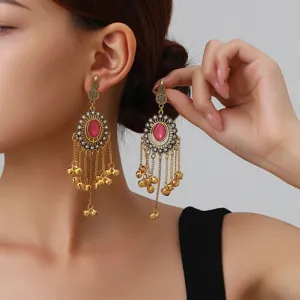 Close-up of ethnic Indian style long tassel bell earrings with pink gemstone and rhinestones.