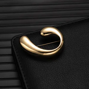 Detailed closeup of a luxurious gold alloy fashion brooch with modern abstract curved design.