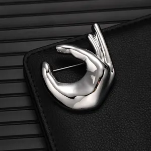 Silver metallic hand gesture brooch detail view, smooth polished alloy fashion accessory.