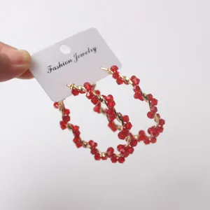 Detail view of red crystal twisted hoop earrings, elegant metallic wrap design for women.