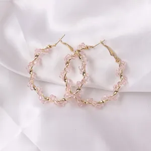 Close-up detail view of elegant pink crystal twisted hoop earrings on soft white satin.