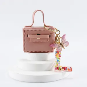 Mini portachiavi borsa in pelle con simpatico farfalla e ciondolo con lettere chic.