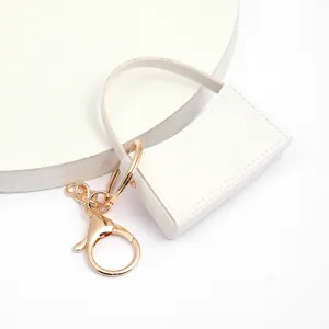 Mini porte-clés sac à main en cuir PU blanc détail avec finitions métalliques dorées et coutures.