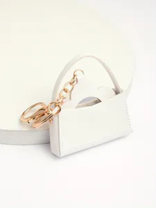 Detail van witte mini handtas sleutelhanger met lederen zakje en gouden metalen ketting.