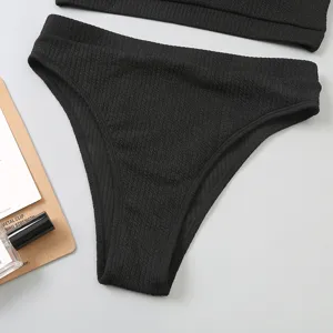 Gros plan sur le détail du bas de bikini taille haute noir en tissu côtelé texturé.