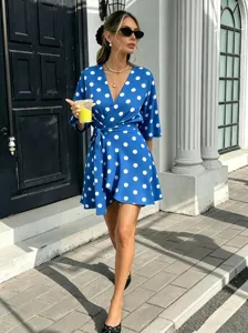 Outdoor street detail view of a blue wrap short dress featuring white polka dots and a V-neck.