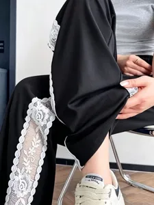 Dettaglio di pantaloni casual neri a gamba larga con elegante finitura in pizzo bianco.