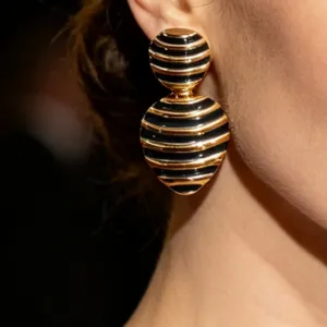 Close-up of vintage black and gold striped enamel drop earrings, elegant retro jewelry detail.