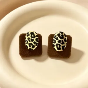 Detalle de pendientes ovalados con estampado de leopardo sobre cojines de terciopelo.