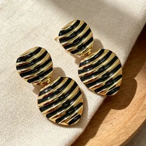 Close-up detail of vintage black and gold striped enamel stud earrings, chic retro design.