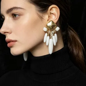 Gros plan detaille des boucles doreilles carrees dores avec des pampilles gouttes blanches.