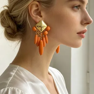 Gros plan de boucles d'oreilles dorées carrées avec pampilles de gouttes orange.