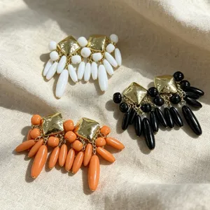 Vue détaillée de boucles d'oreilles pendantes colorées avec clous carrés dorés et perles.