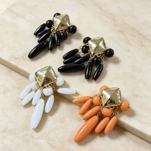 Gros plan de boucles d'oreilles à pampilles en résine avec clou carré doré élégant.