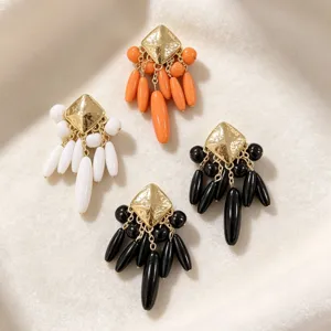 Détail en gros plan de boucles d'oreilles rétro géométriques à clous carrés et pampilles de perles.