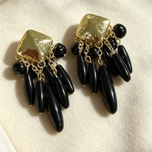 Gros plan de boucles d'oreilles vintage dorées à carré supérieur et pampilles de perles noires.