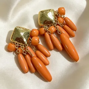 Gros plan détaillé de boucles d'oreilles pendantes orange style vintage avec clous carrés.