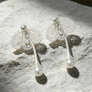Gros plan détaillé de boucles d'oreilles élégantes en dentelle argentée et perles sur pierre.