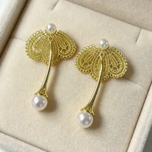Gros-plan de boucles d'oreilles perles dorées au design de éventail en dentelle délicate.