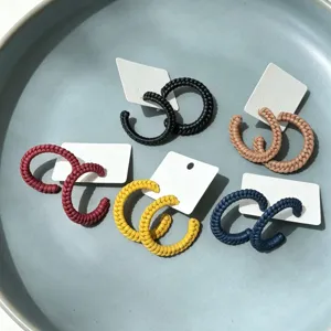 Gedetailleerde close-up van stijlvolle gevlochten lederen C-hoop oorbellen in kleuren.
