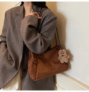 Detail view of brown suede shoulder bag featuring cute bear pendant and stylish logo.