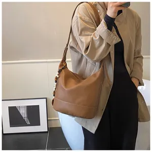Retro brown leather shoulder bucket bag detail showcasing elegant stitching and beaded charm.