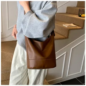 Detail shot of a brown leather bucket shoulder bag worn on stairs, retro fashion style.