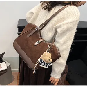 Gros plan sur le sac cabas d'epaule en sude marron avec fermoir metallique et charm de chien.