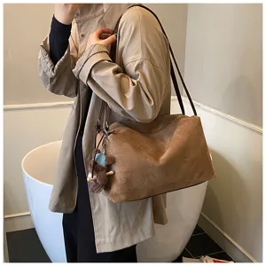 Brown suede shoulder bag detail showing soft texture, slender strap, and cute bear pendant.