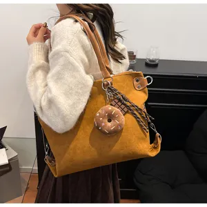 Detailed view of brown suede tote bag with cute plush doughnut charm and shoulder straps.