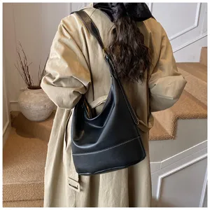 Detailed view of a stylish black bucket shoulder bag worn on a trench coat in a chic indoor setting.