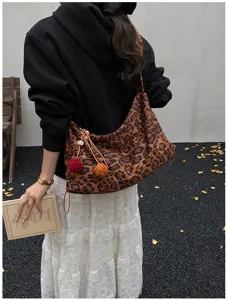 Detailed view of the retro leopard print slouchy shoulder bag with cute fluffy pom-pom charms.