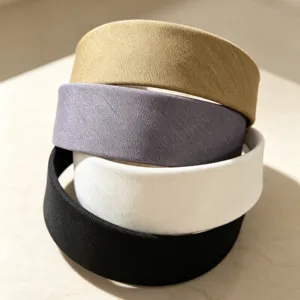 Detailed view of four retro fabric wide headbands stacked together in khaki, grey, white, and black.