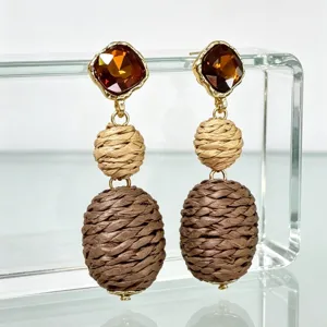 Close-up of bohemian style retro drop earrings featuring brown crystal and woven straw balls.
