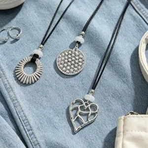 Detail shot of three silver hollow metal pendants with black cord on denim background.
