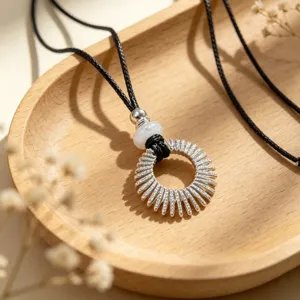 Detailed shot of a silver openwork circle pendant necklace with black cord and beads on wood tray.