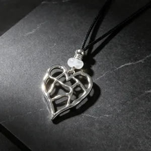 Close-up of silver hollow heart pendant necklace with black cord on dark slate background.